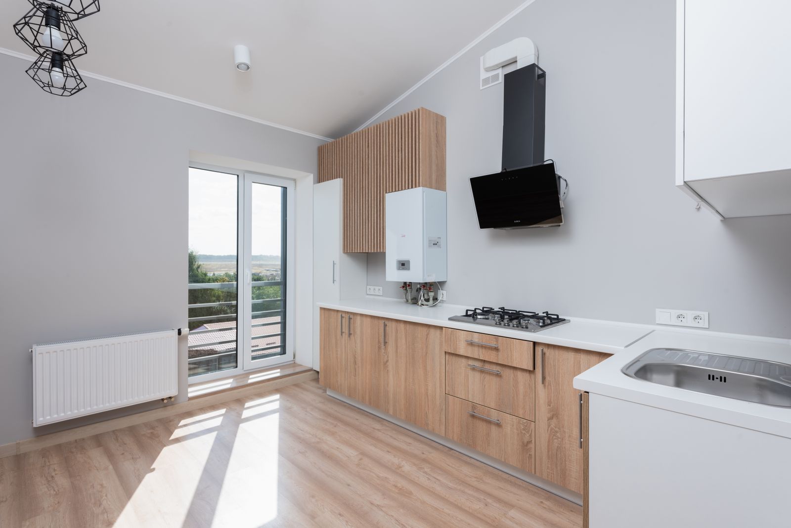 Galley kitchen with light wood fronts, white countertop and balcony door