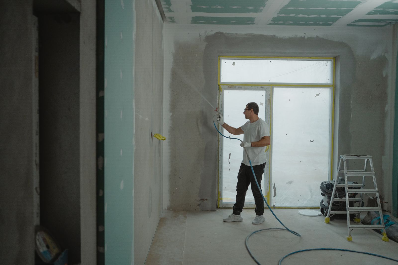 Painter spraying freshly finished drywall walls